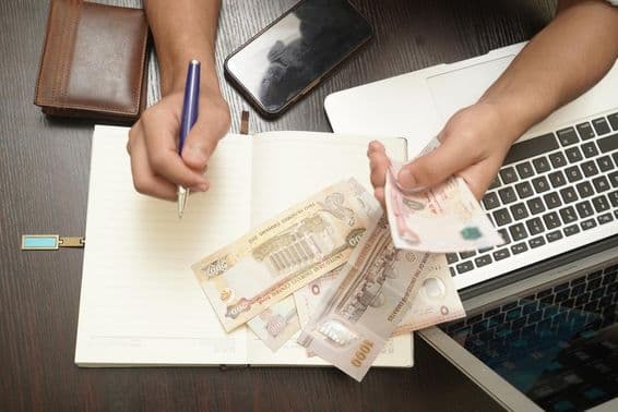 Un homme comptant une liasse de billets de dirhams des Émirats Arabes Unis.