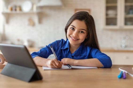 Écolière heureuse suivant des cours à la maison sur une tablette.