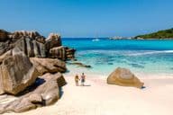 Deux voyageurs marchant sur les sables blancs et doux de la plage d'Anse Cocos aux Seychelles.