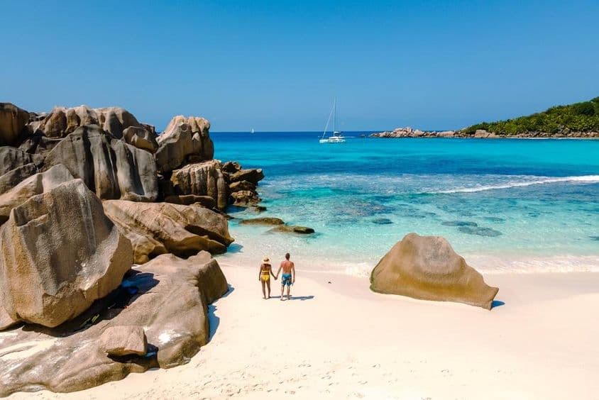 Deux voyageurs marchant sur les sables blancs et doux de la plage d'Anse Cocos aux Seychelles.